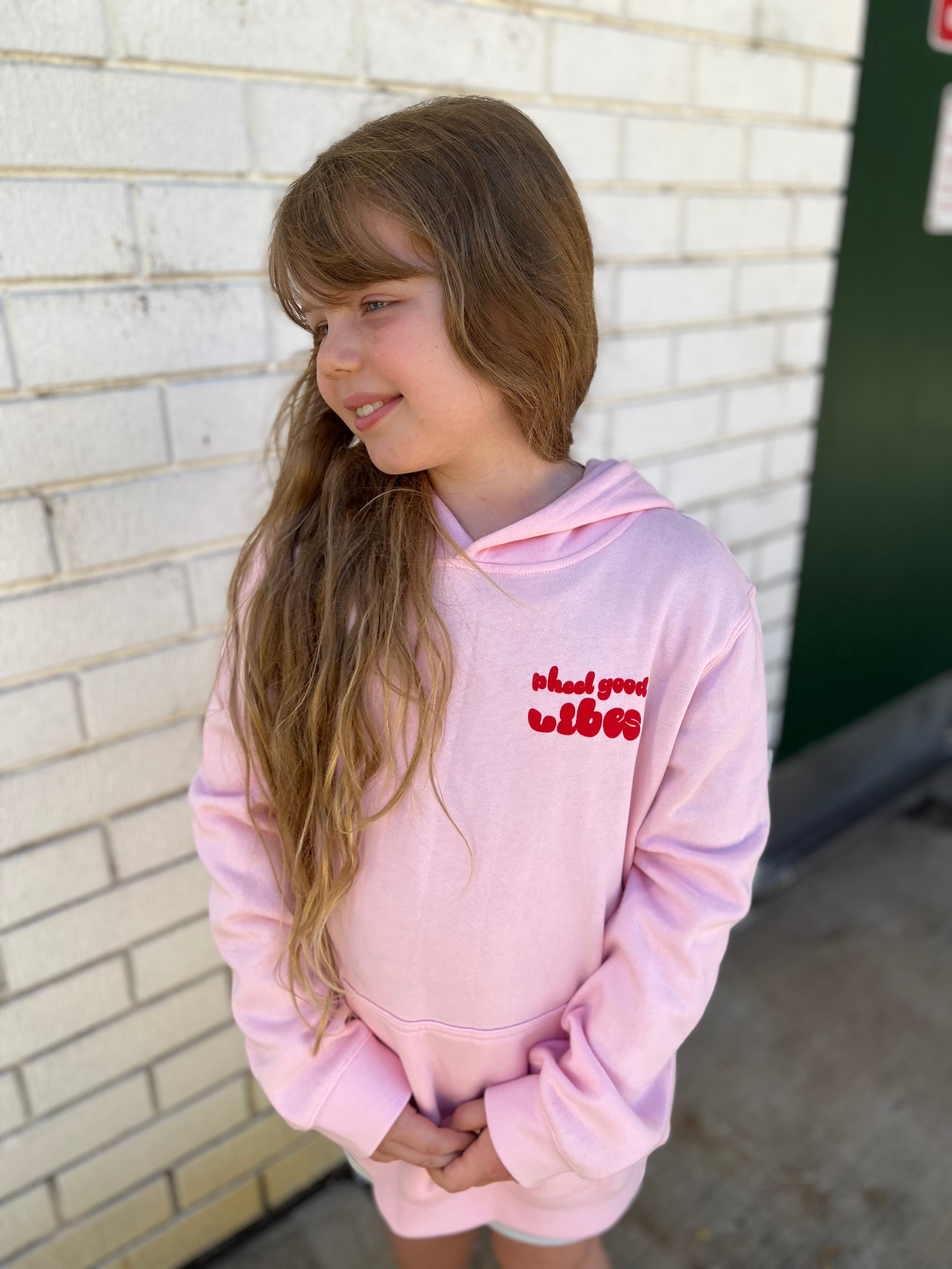 Blonde girl in comfy pink pheels hoodle with red "pheel good vibes" logo